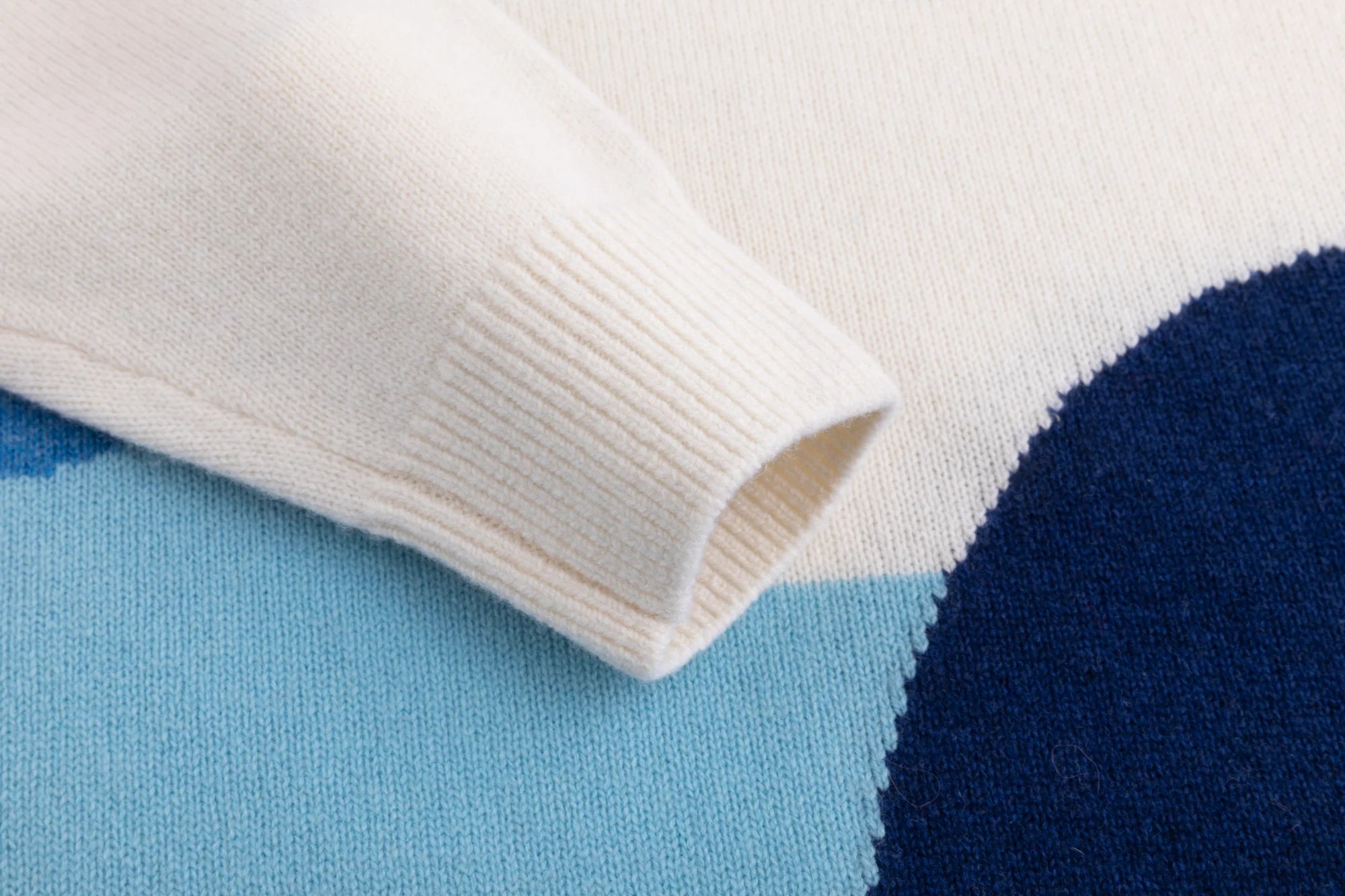Close-up of the ribbed cuff and contrasting pale blue sleeve panel on the cream jumper.