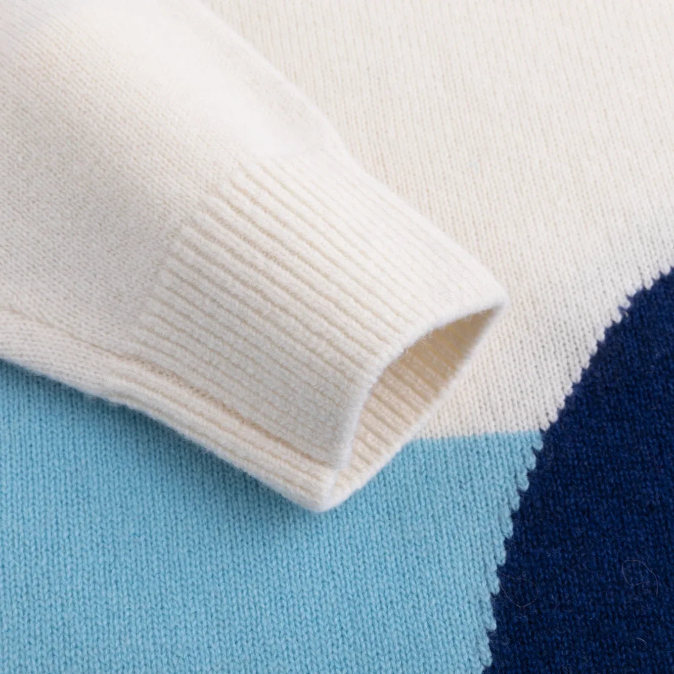 Close-up of the ivory ribbed cuff beside the blue and navy intarsia.