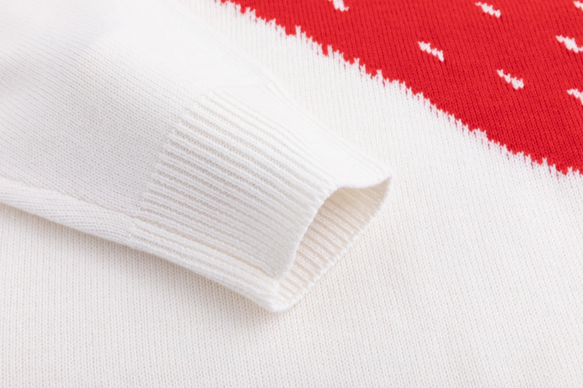 Close-up of the ribbed cuff beside the red intarsia on the ivory jumper.