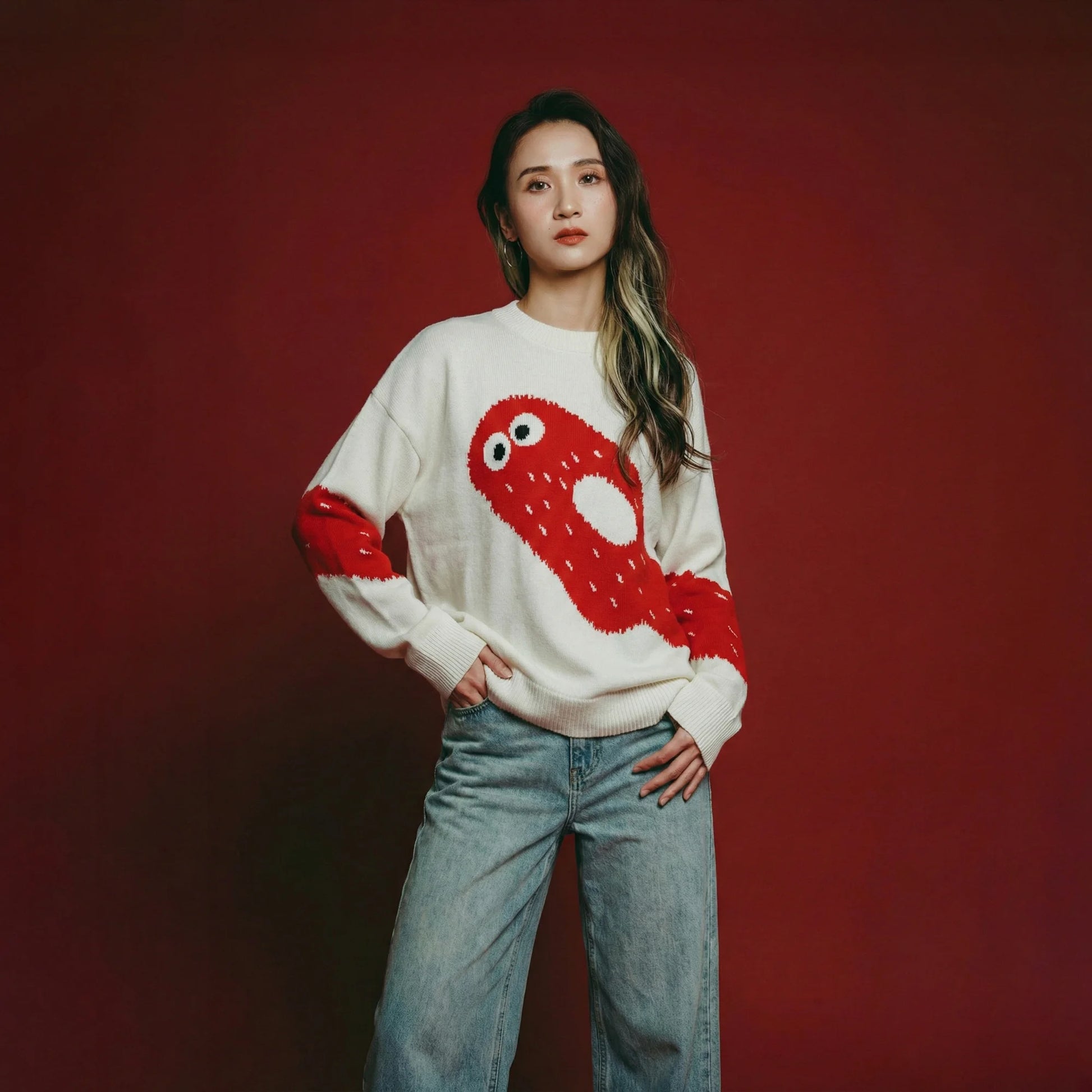 Woman wearing an ivory cotton and wool blend jumper with a cute red ghost intarsia across the front and sleeves.
