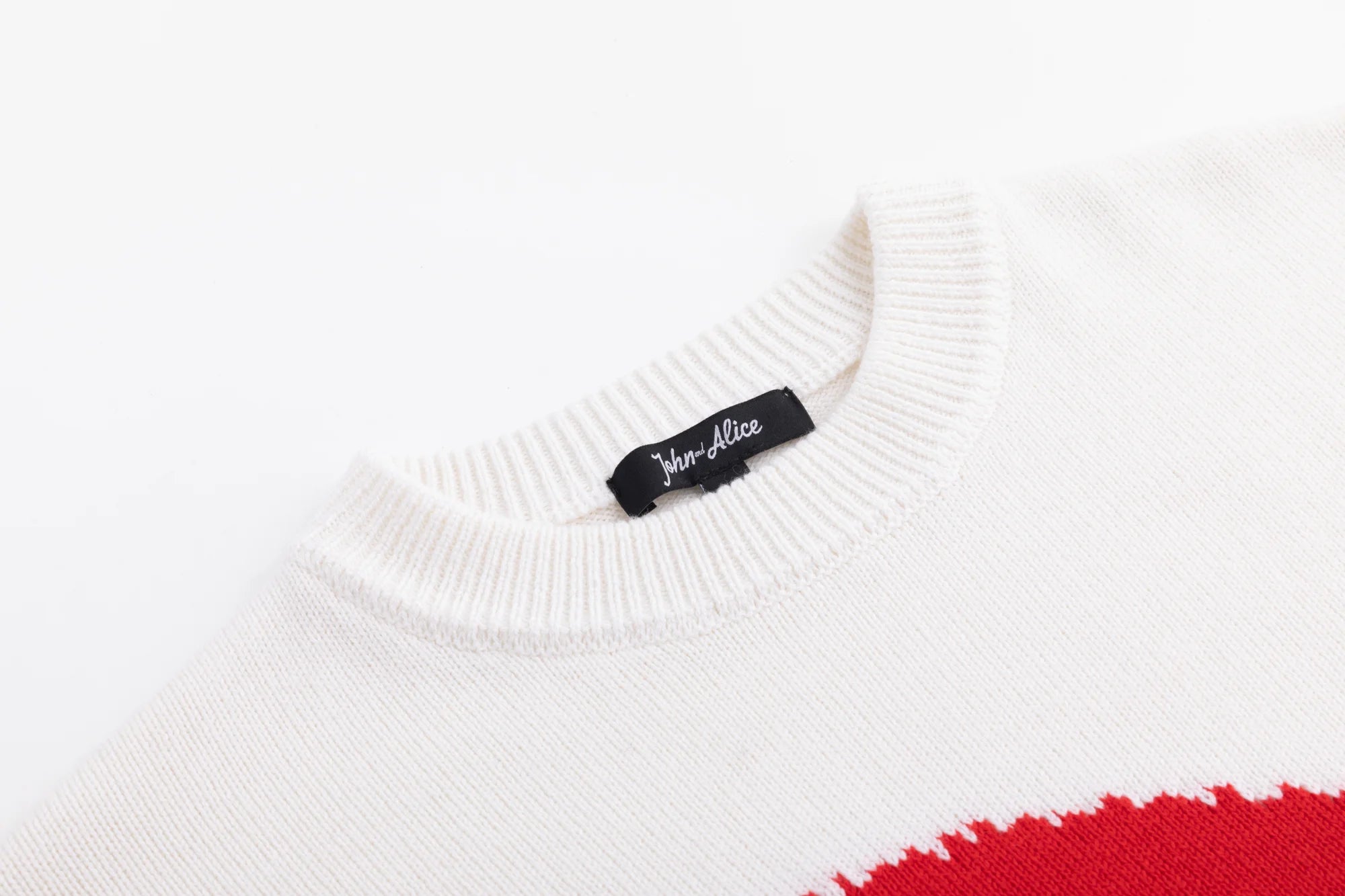 Close-up of the ribbed crew neckline on the ivory jumper with part of the red intarsia visible.
