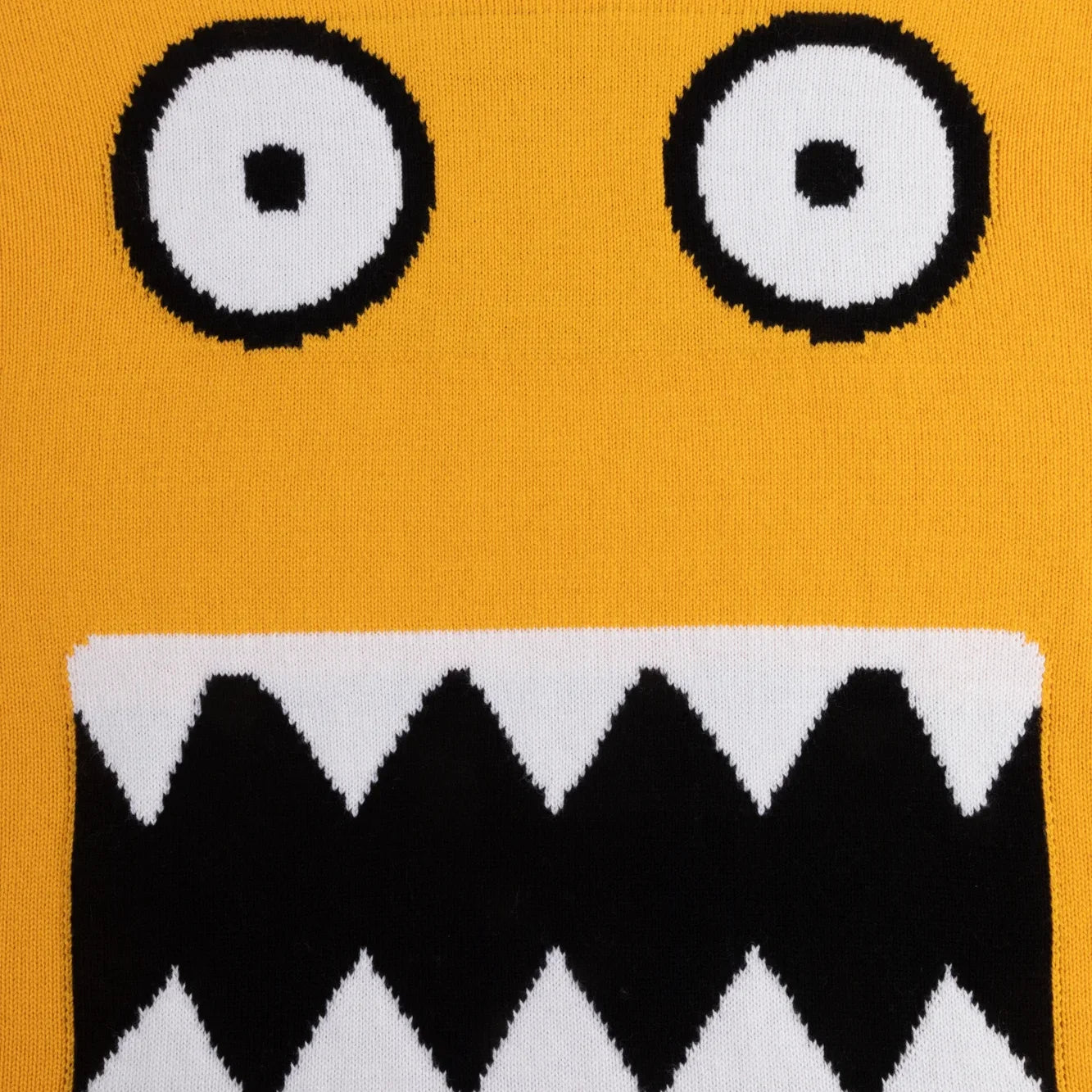 Black and white monster eyes and jagged mouth knitted on yellow