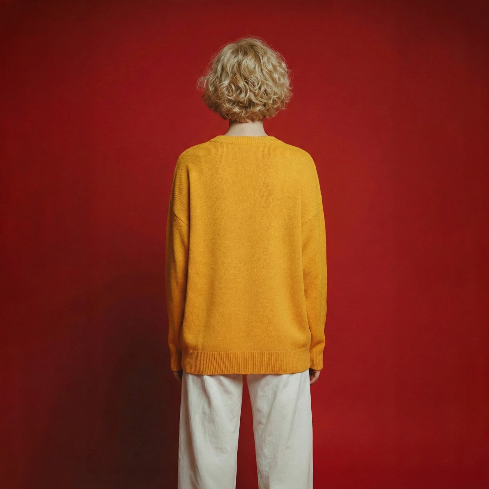 Back view of model wearing a mustard yellow cotton and wool blend jumper with an oversized dropped-shoulder fit.