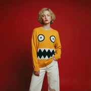 Model wearing a mustard yellow cotton and wool blend jumper with a monster face jacquard on the front and an oversized dropped-shoulder fit.