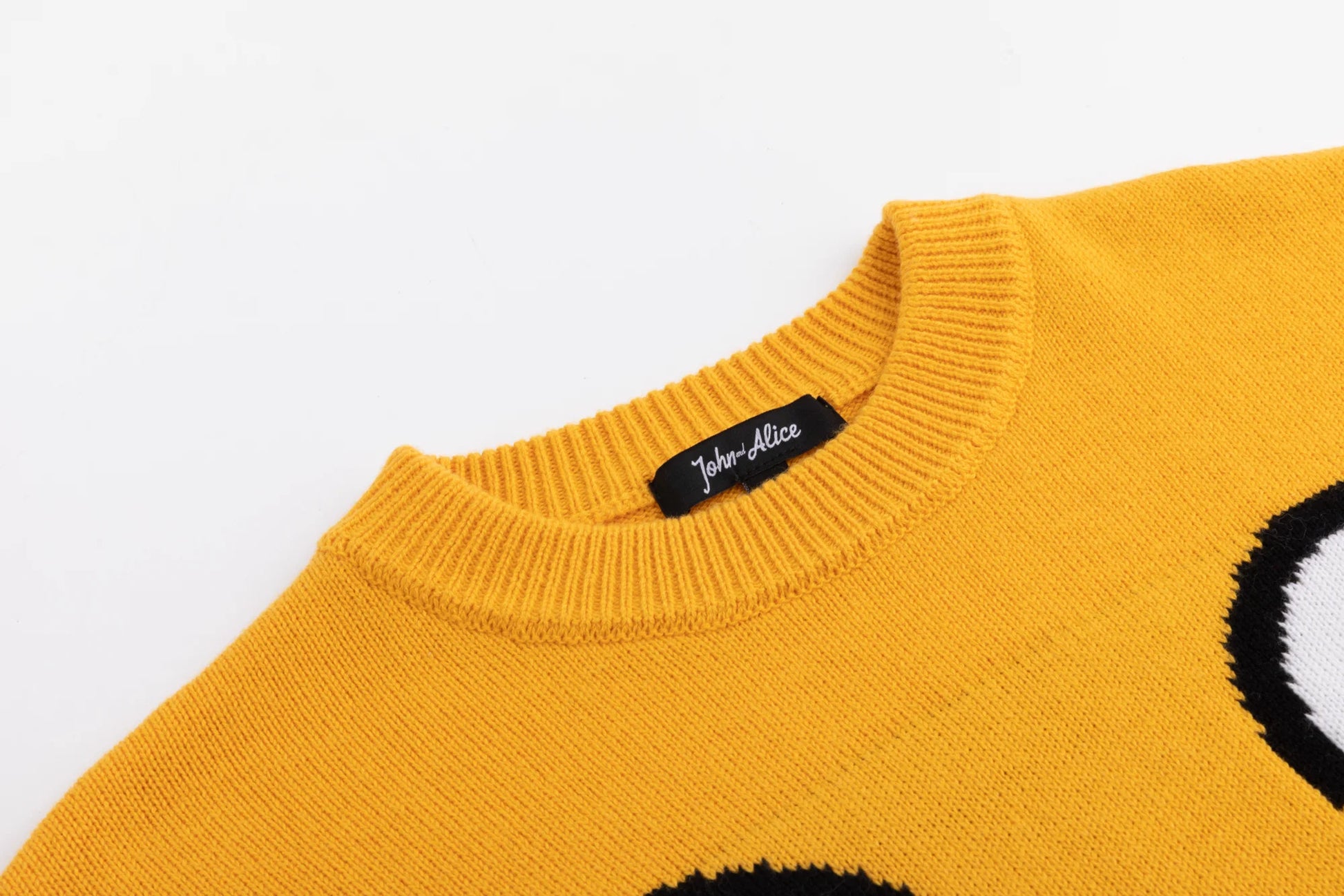 Close-up of the ribbed crew neckline on the mustard yellow jumper with part of the monster motif visible.