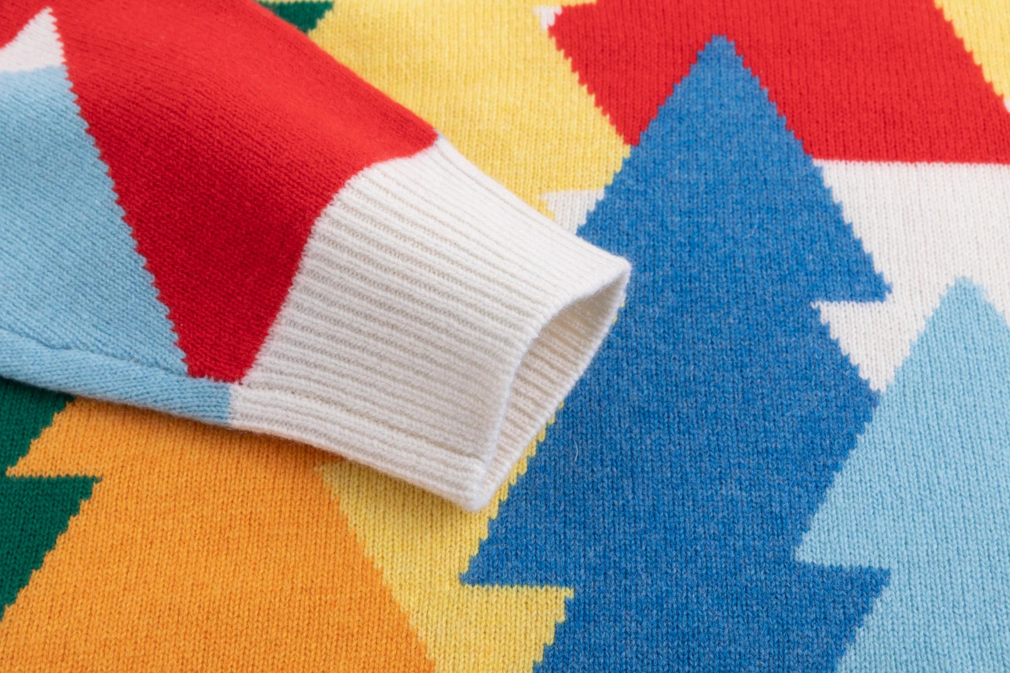 Close-up of the ribbed cuff beside the multicolour forest intarsia on the ivory jumper.
