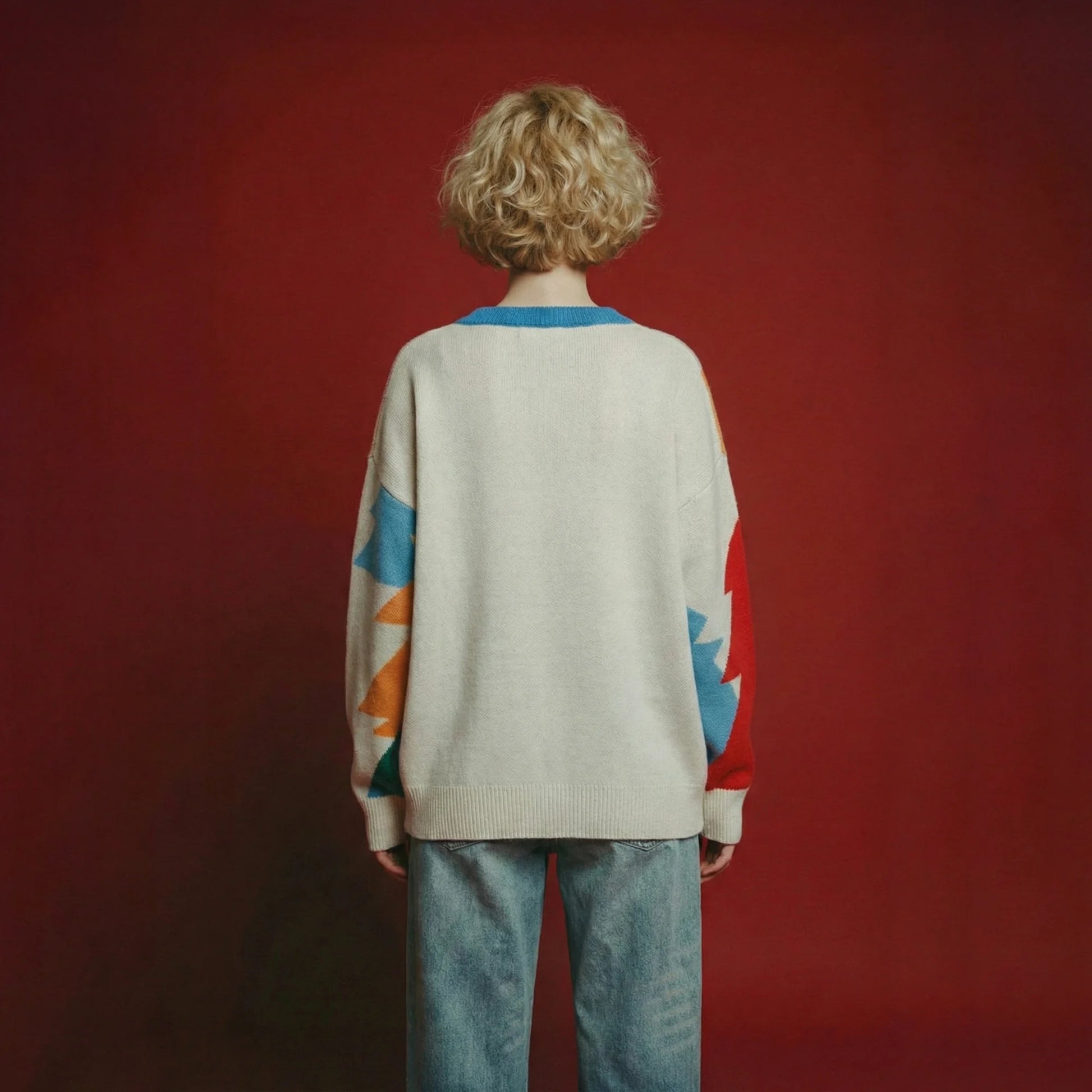Back view of model wearing an ivory merino wool jumper with multicolour forest intarsia on the sleeves and an oversized dropped-shoulder fit.