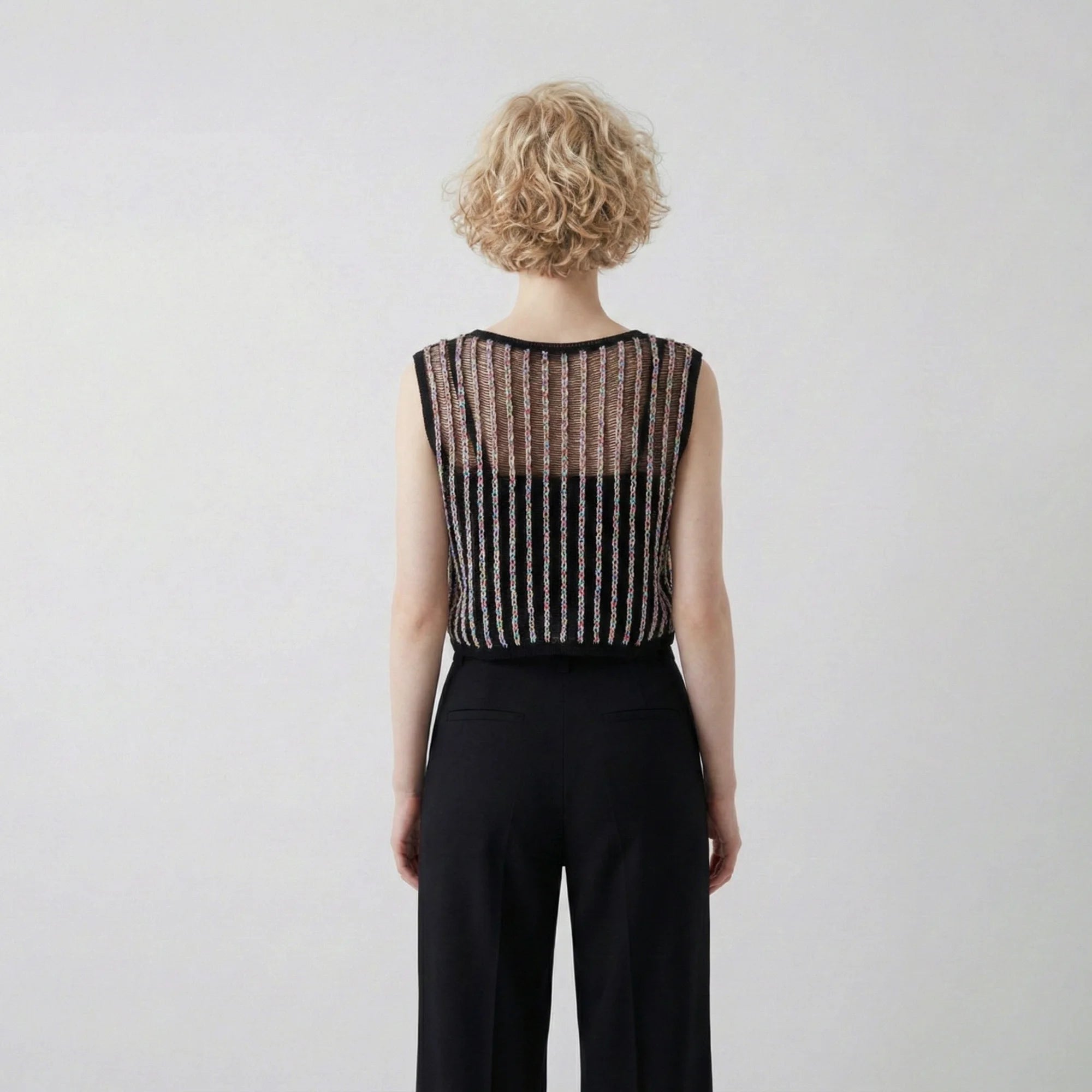 Back view of model wearing a black crochet top with multicolour vertical stripes and a sleeveless cropped silhouette.