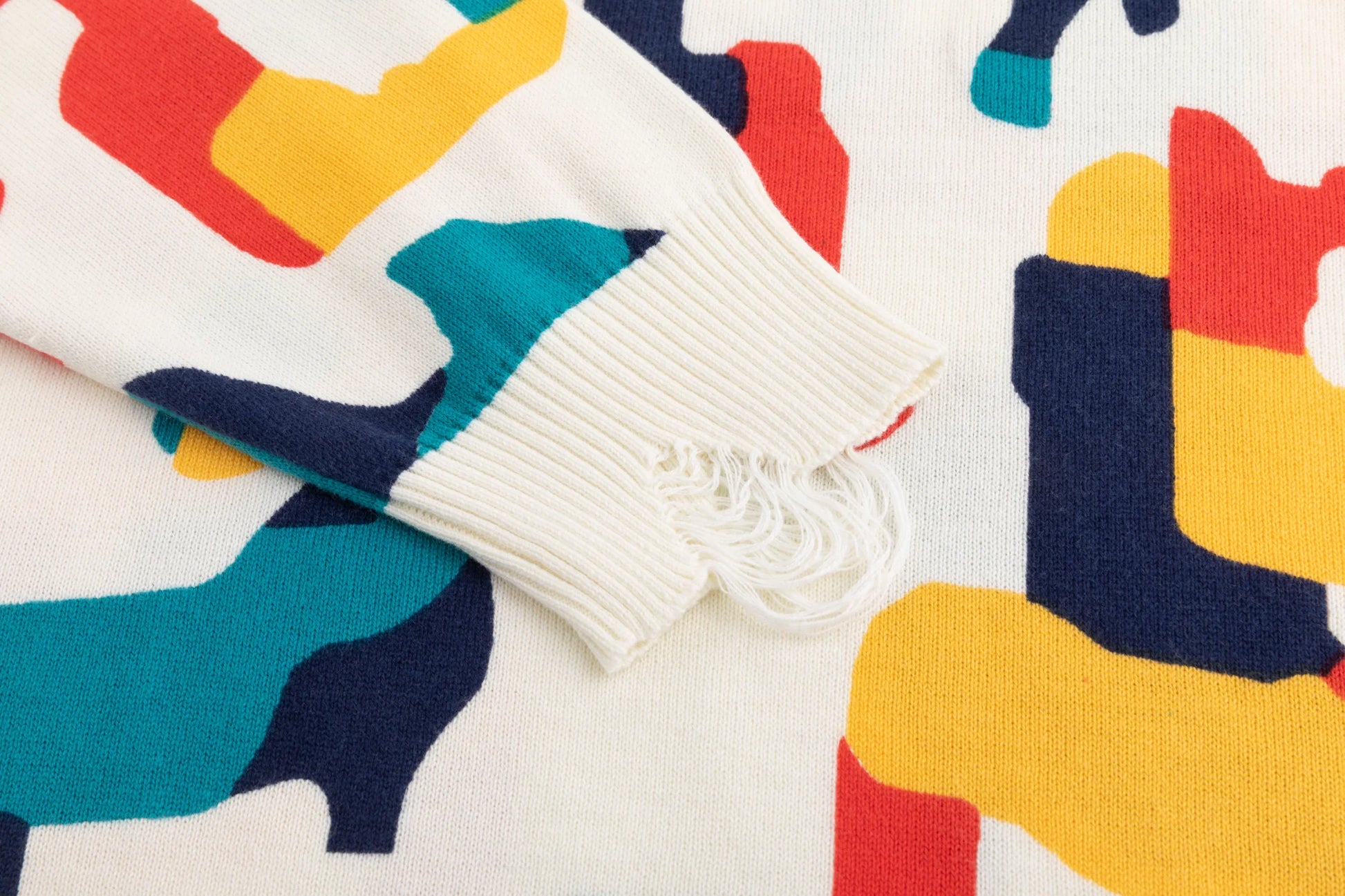 Close-up of the distressed ribbed cuff on the ivory jumper with the abstract horse print beside it.
