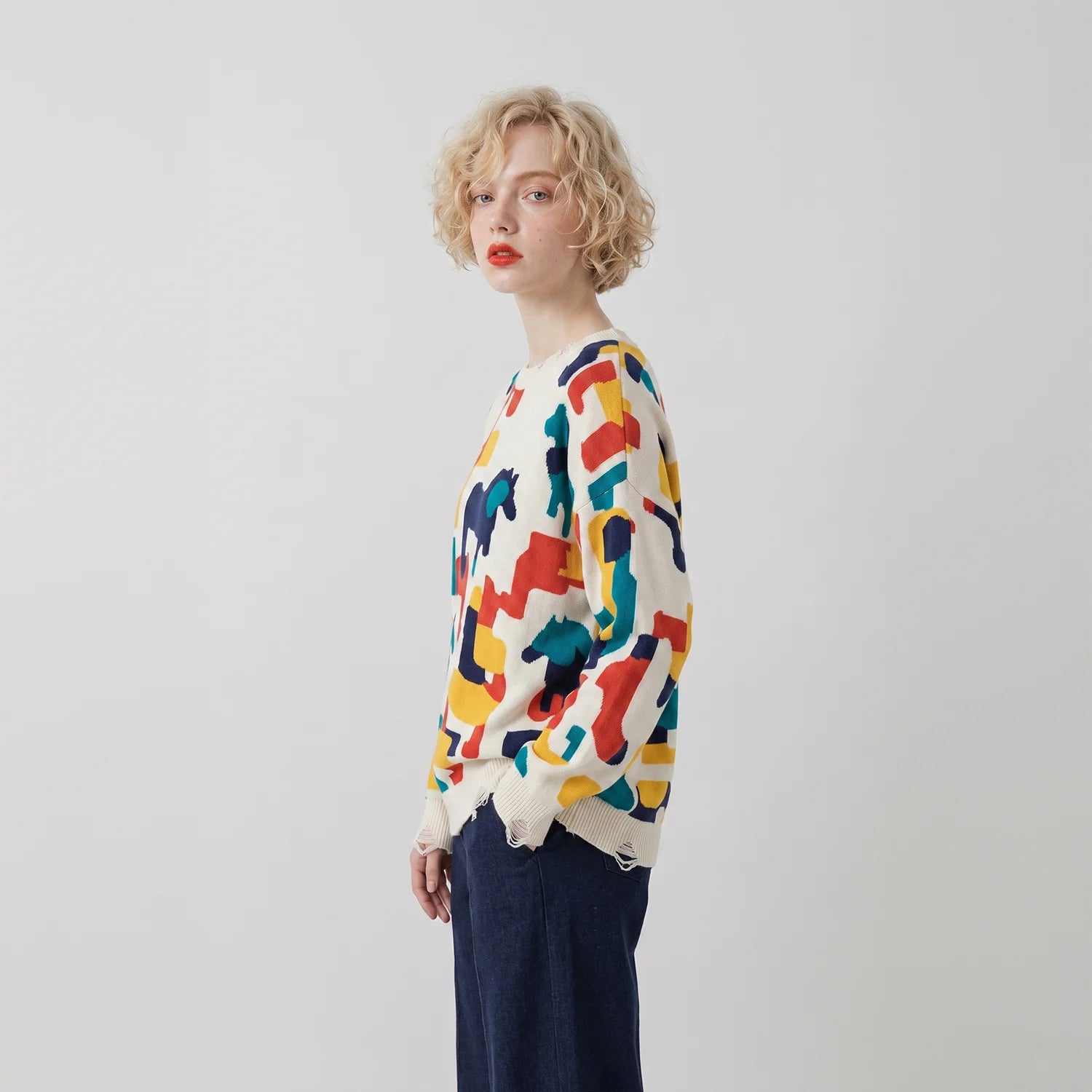 Side view of model wearing an ivory jumper with a multicolour abstract horse print.