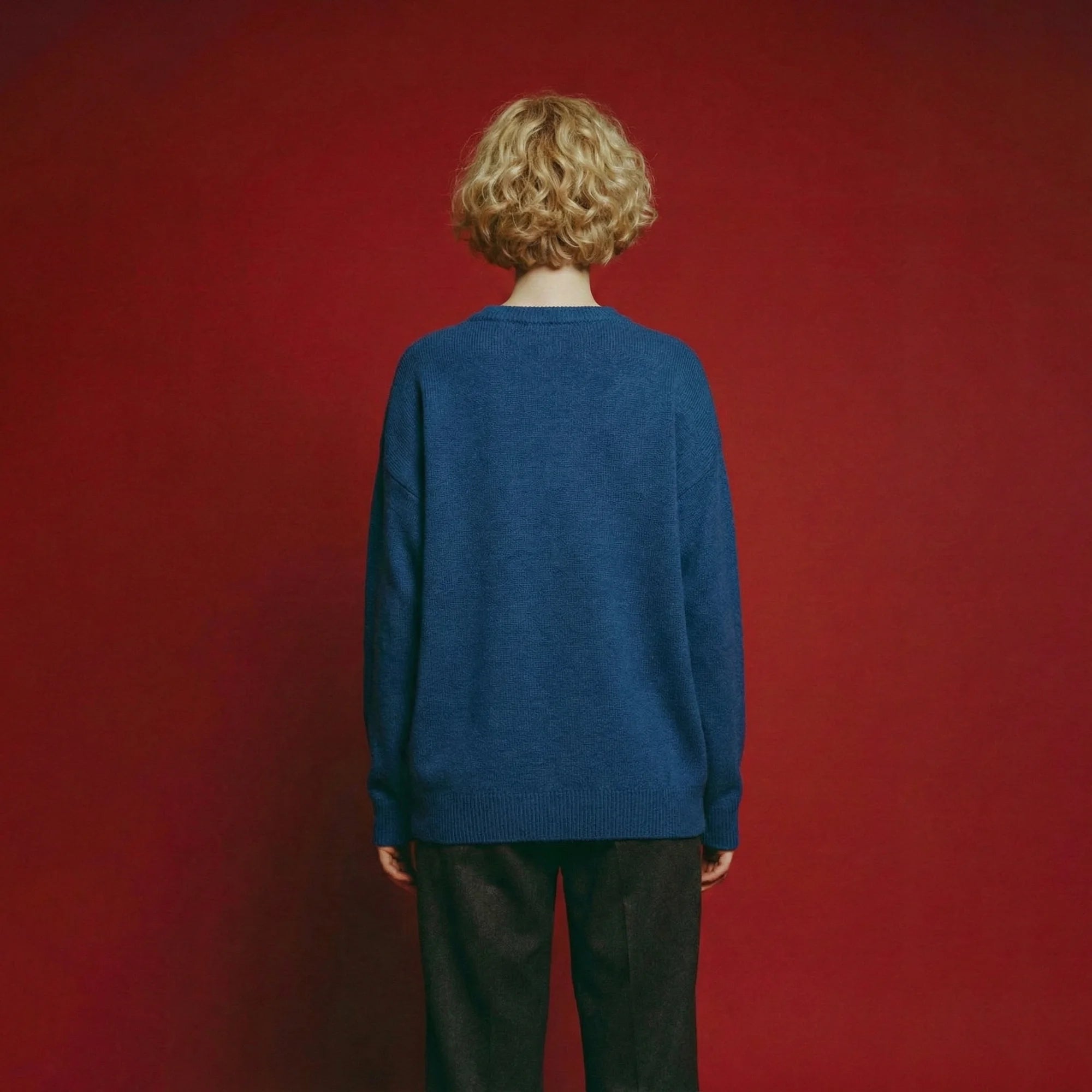 Back view of model wearing a blue merino wool jumper with an oversized dropped-shoulder fit.