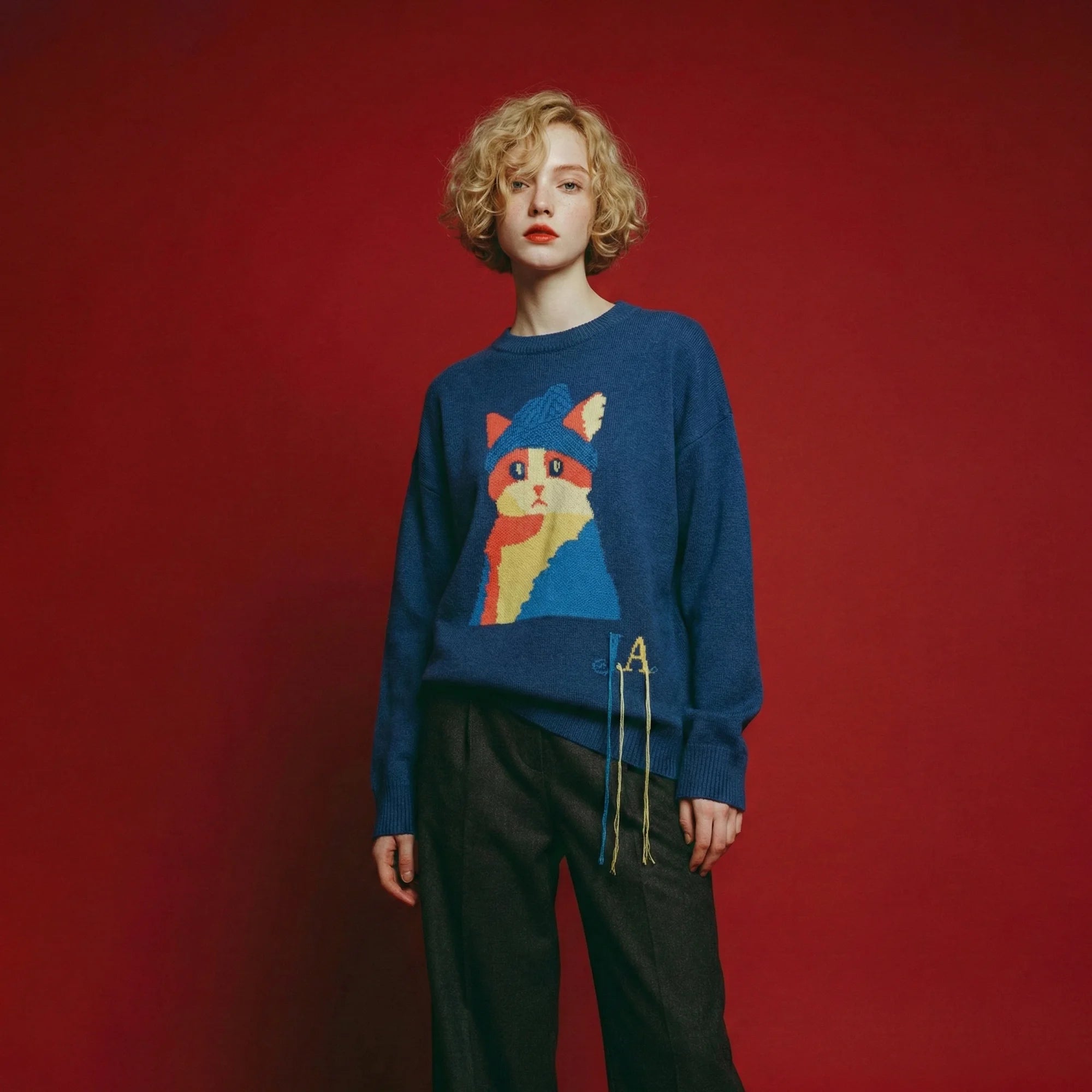Model wearing a blue merino wool jumper with an artistic cat intarsia on the front and an oversized dropped-shoulder fit.