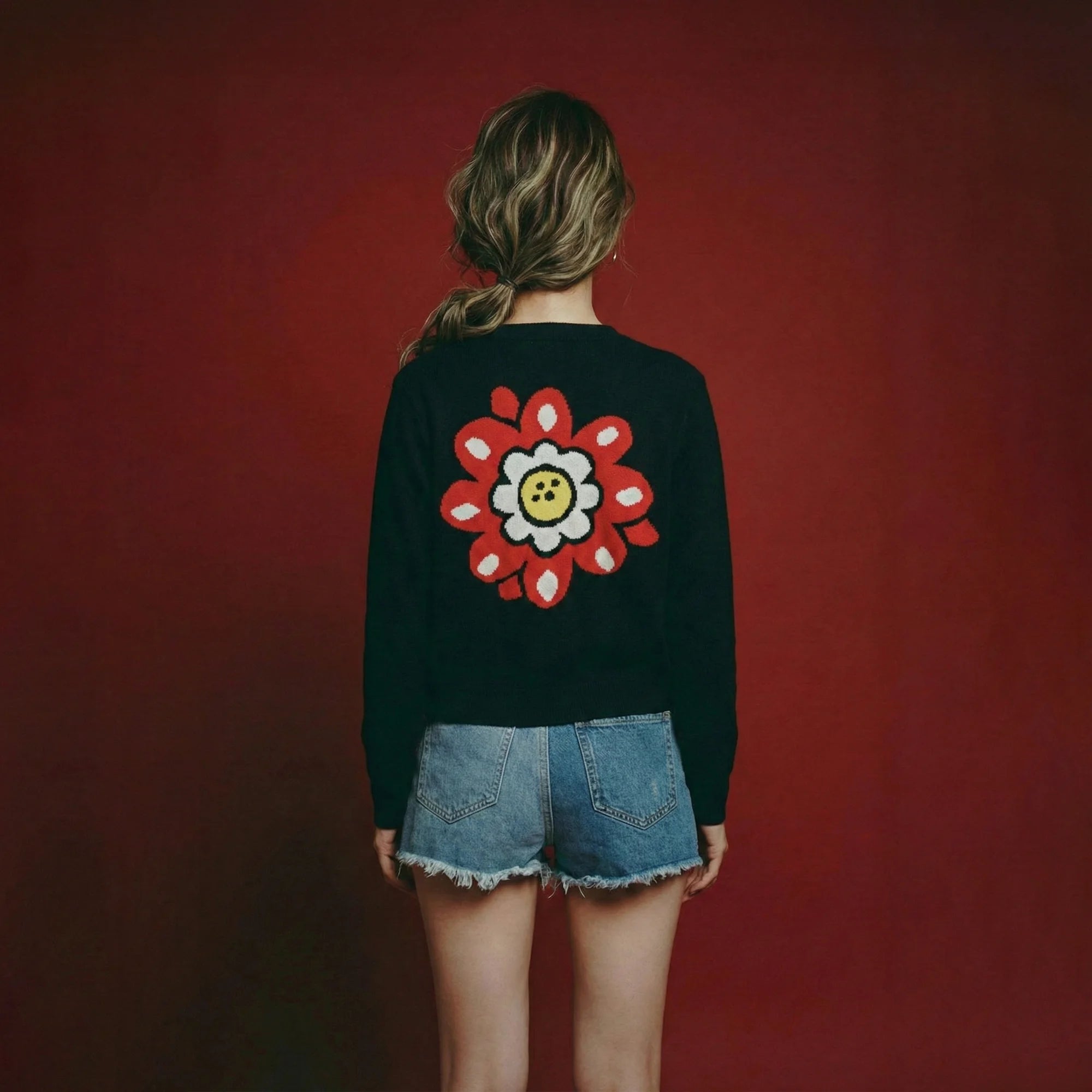 Back view of model wearing a black cropped cardigan with a large floral intarsia on the back.