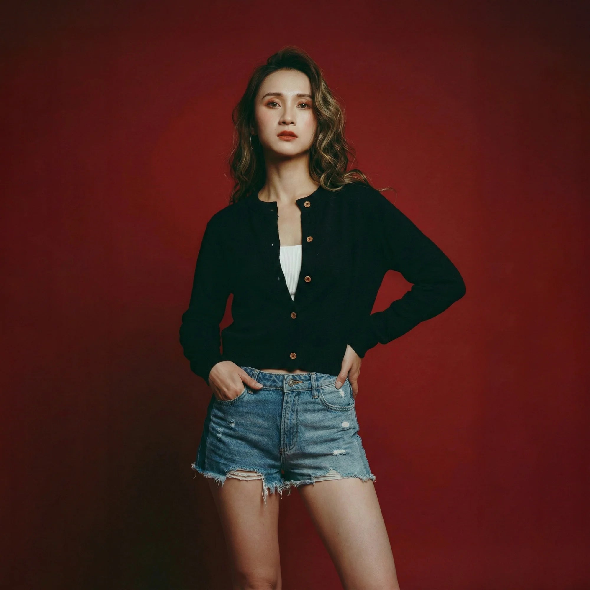 Model wearing a black cropped cardigan with a round neckline, dropped shoulders and wood buttons.