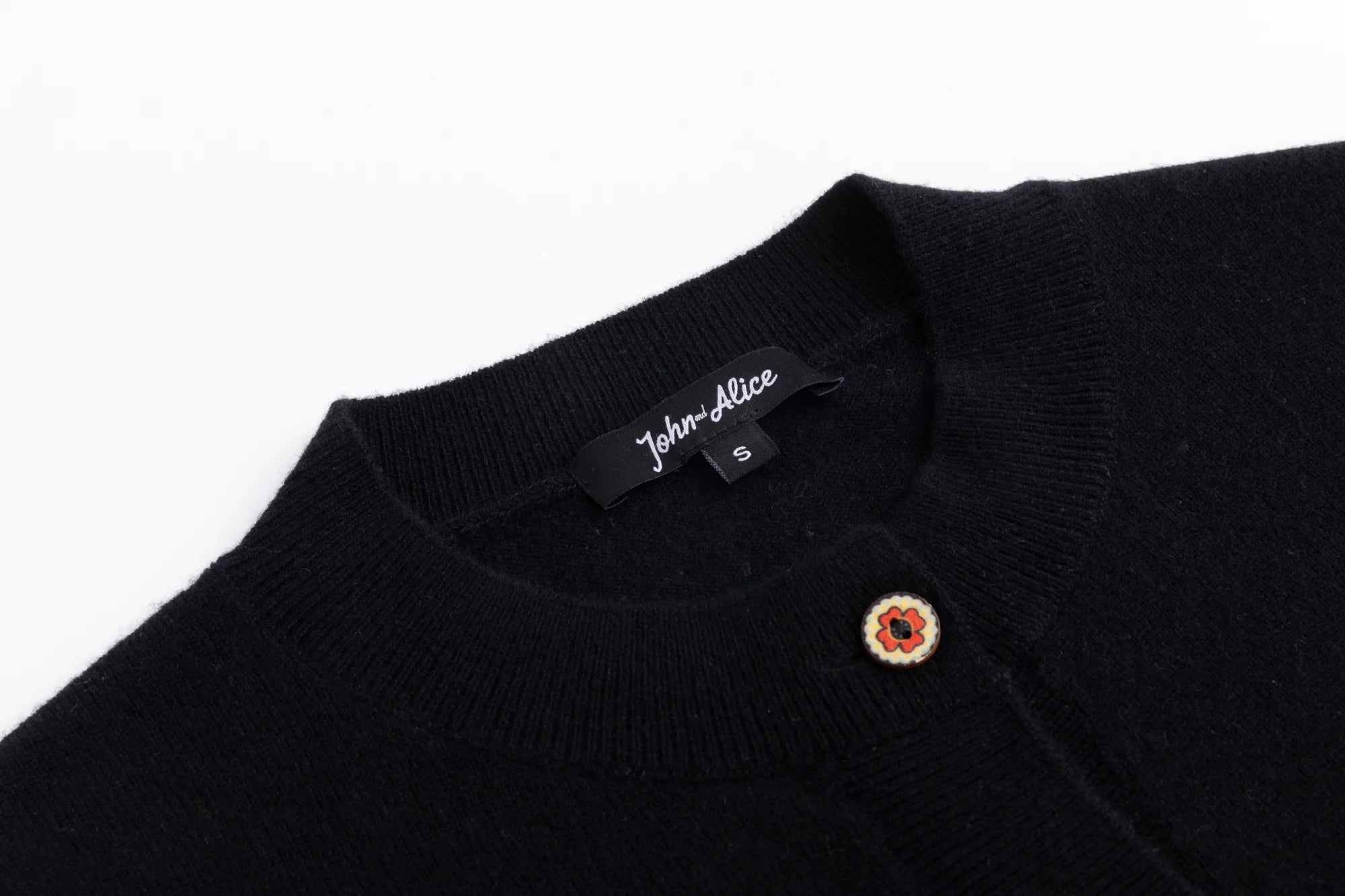 Close-up of the round neckline on the black cardigan with part of the button placket visible.