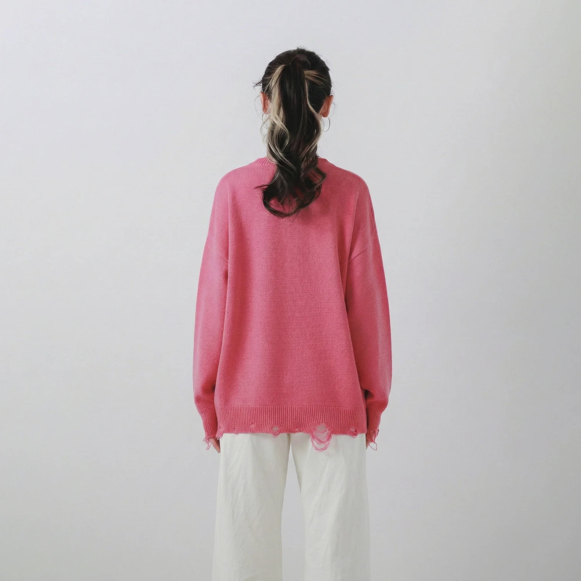 Back view of model wearing a pink merino wool jumper with an oversized dropped-shoulder fit and distressed ribbed trims.