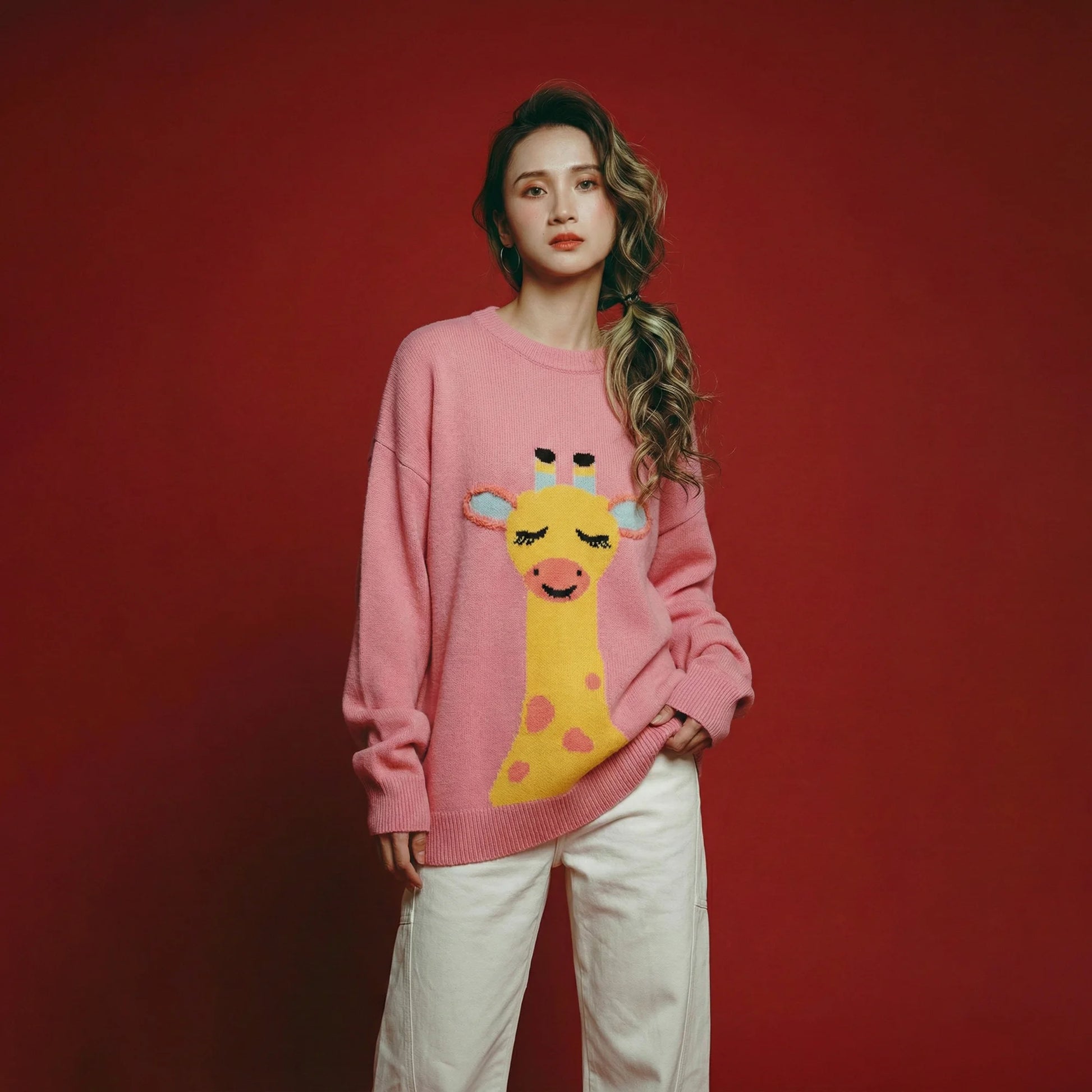 Model wearing a pink merino wool jumper with a giraffe intarsia on the front and an oversized dropped-shoulder fit.